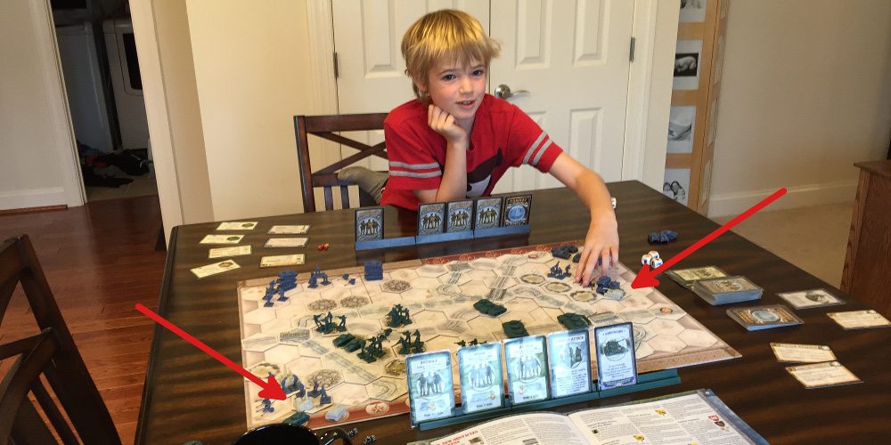 Child sitting in front of a set up game of Memoir '44 showing the unpainted Equipment Pack pieces.