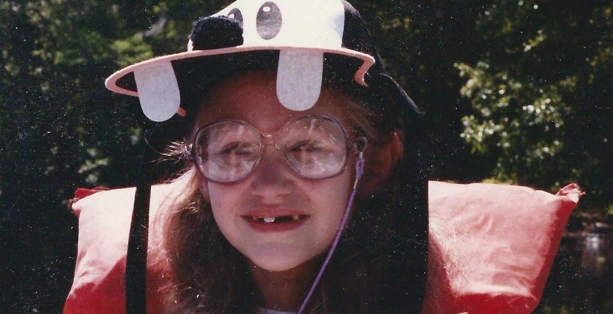 Young girl with large glasses and a Goofy hat in a life vest.