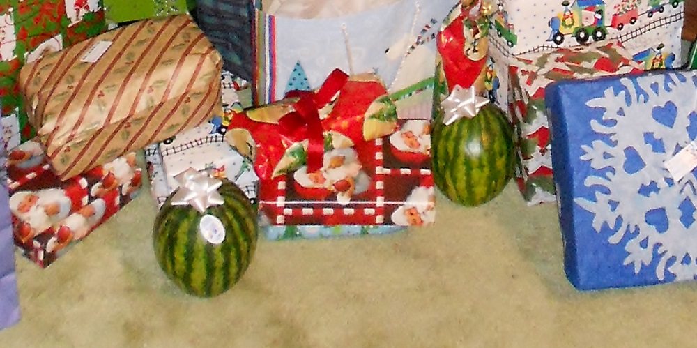 two "baby" watermelon with bows sitting among other wrapped gifts