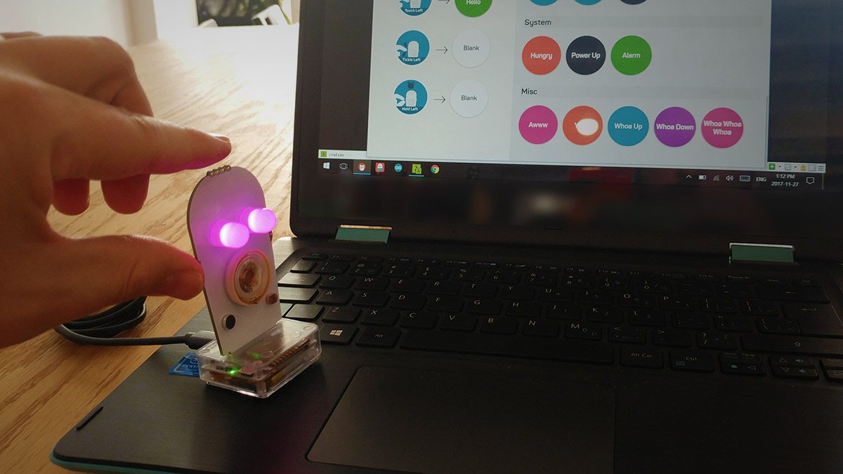 Little Robot Friends with pink eye LEDs, sitting on laptop