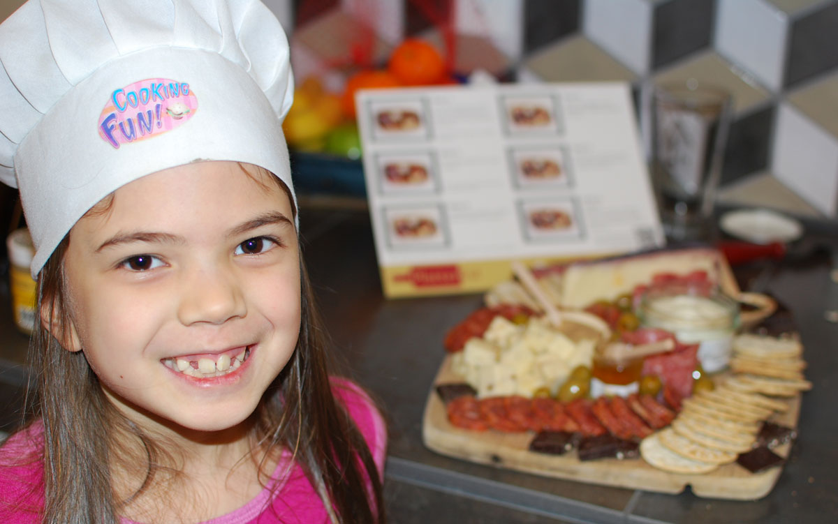 Daughter wearing chef's hat, next to finished charcuterie tray